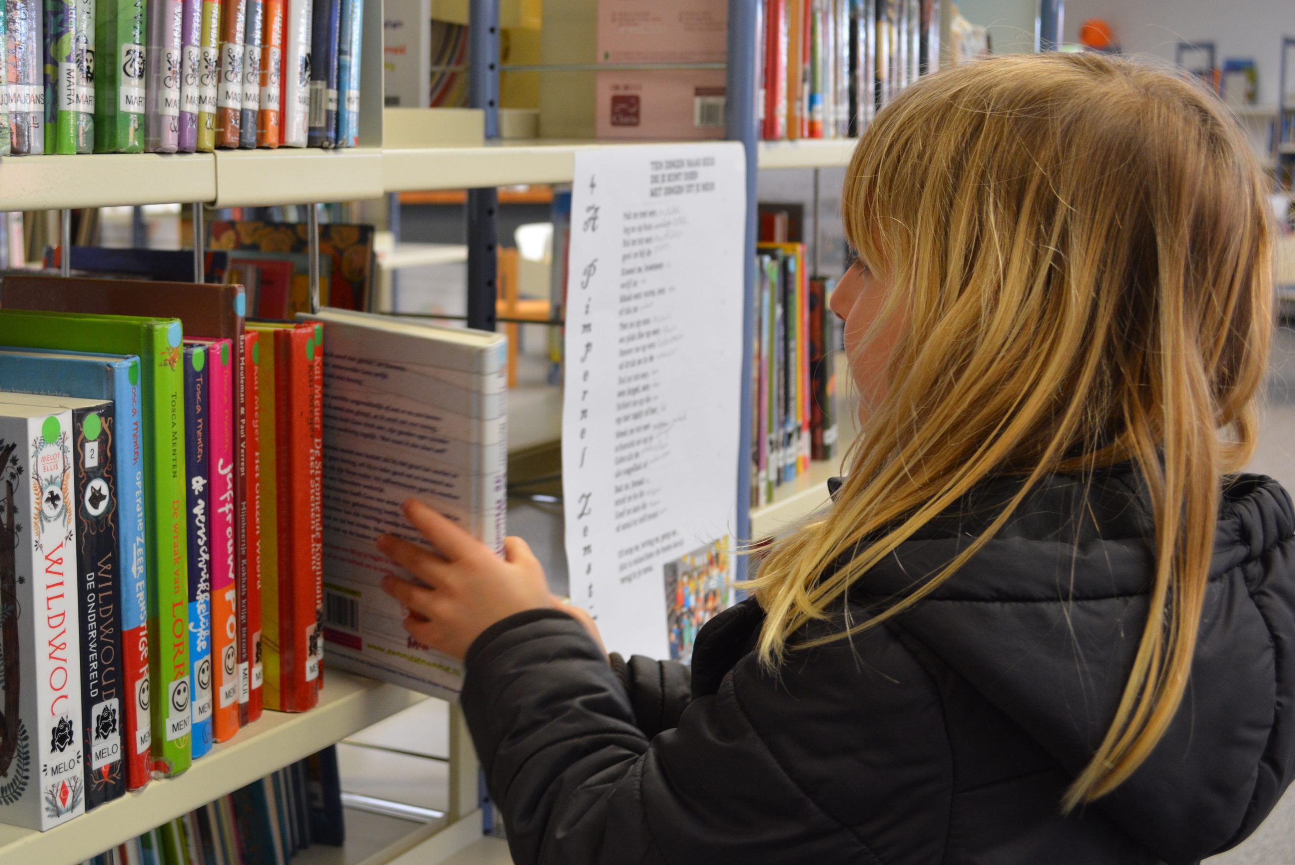 little girl pulling book from library shelf