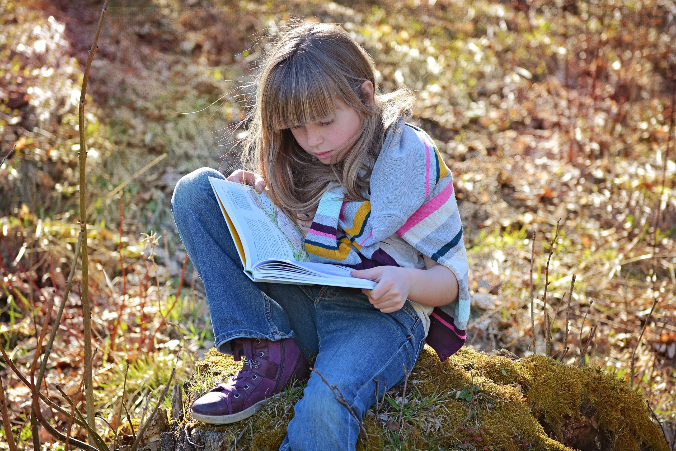 girl sitting on rock reading a book