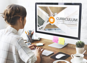 woman in front of computer screen reading "Curriculum"