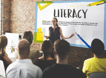 woman presenting in front of board with big literacy heading