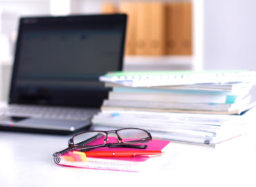 work desk with paper, laptop, and glasses