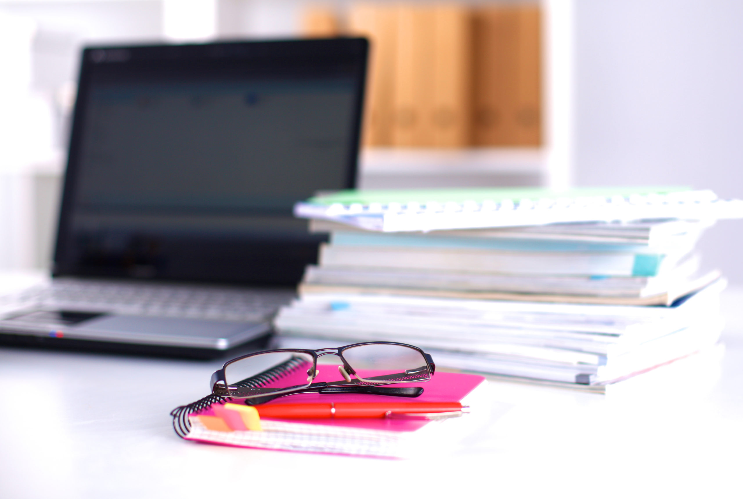 work desk with paper, laptop, and glasses